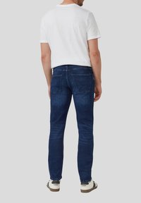 Ciemnoniebieskie dżinsy slim fit z tylnymi kieszeniami, w połączeniu z gładką białą koszulą z krótkim rękawem. Ubrane z casualowymi trampkami.