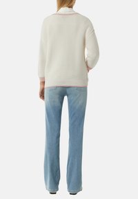 Witte gebreide trui met roze accenten, comfortabele pasvorm en driekwart mouwen, gecombineerd met lichtblauwe flared jeans die iets vervaagd zijn bij de dijen.
