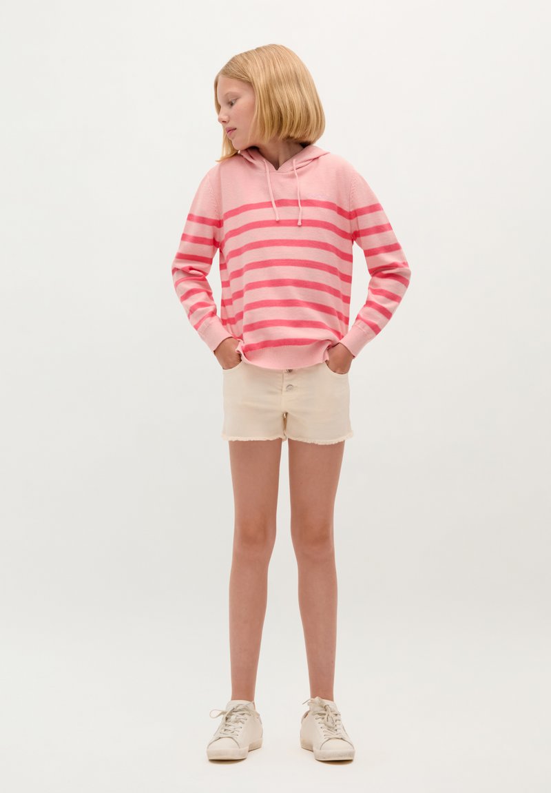 Haut à capuche rose rayé avec cordon de serrage, associé à un short en denim couleur crème. Des baskets blanches complètent cette tenue décontractée.