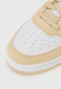 Sneaker beige in suede e pelle bianca con punta perforata, lacci rotondi e suola in gomma bianca con un sottile accento color gomma.
