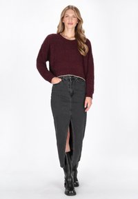 Burgundowa, puszysta dzianinowa sweter, spódnica z czarnego denimu o wysokim stanie z przednim rozcięciem, w połączeniu z wysokimi, czarnymi skórzanymi butami do kolan.