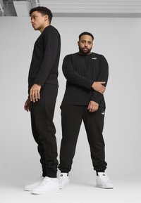 Sorte langærmede skjorter og sweatpants lavet af blødt stof, parret med hvide sneakers. Indeholder Puma-logo på skjorterne og bukserne.