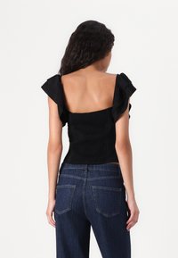 Svart smocketopp med volangerm sleeves. Har en tettsittende design som eksponerer ryggen, kombinert med høy midje mørk denim jeans.
