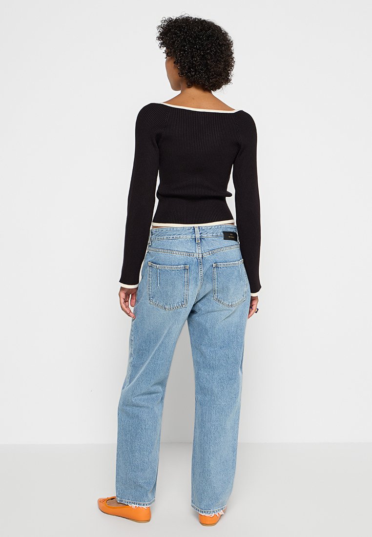 Schwarzes, geripptes Langarm-Oberteil mit eckigem Ausschnitt, kombiniert mit blauen, hochgeschnittenen Jeans aus Denim in lockerer Passform und zwei Gesäßtaschen.