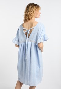 Lichtblauwe jurk met korte gerafelde mouwen, verticale strepen, kantafwerking in de taille, en een open rug die met een strik is vastgebonden. Zachte, gestructureerde stof.