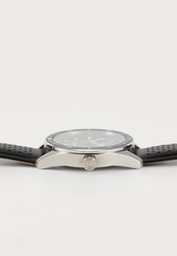 Relógio masculino com bracelete de silicone preto, caixa em aço inoxidável prateado, mostrador preto e marcadores de horas luminescentes. Possui um display de data e coroa.