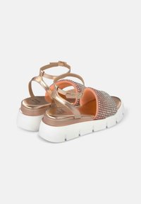Sandales plateforme en rose doré avec des détails en strass scintillants sur la sangle, une sangle de cheville ajustable et une semelle texturée blanche.