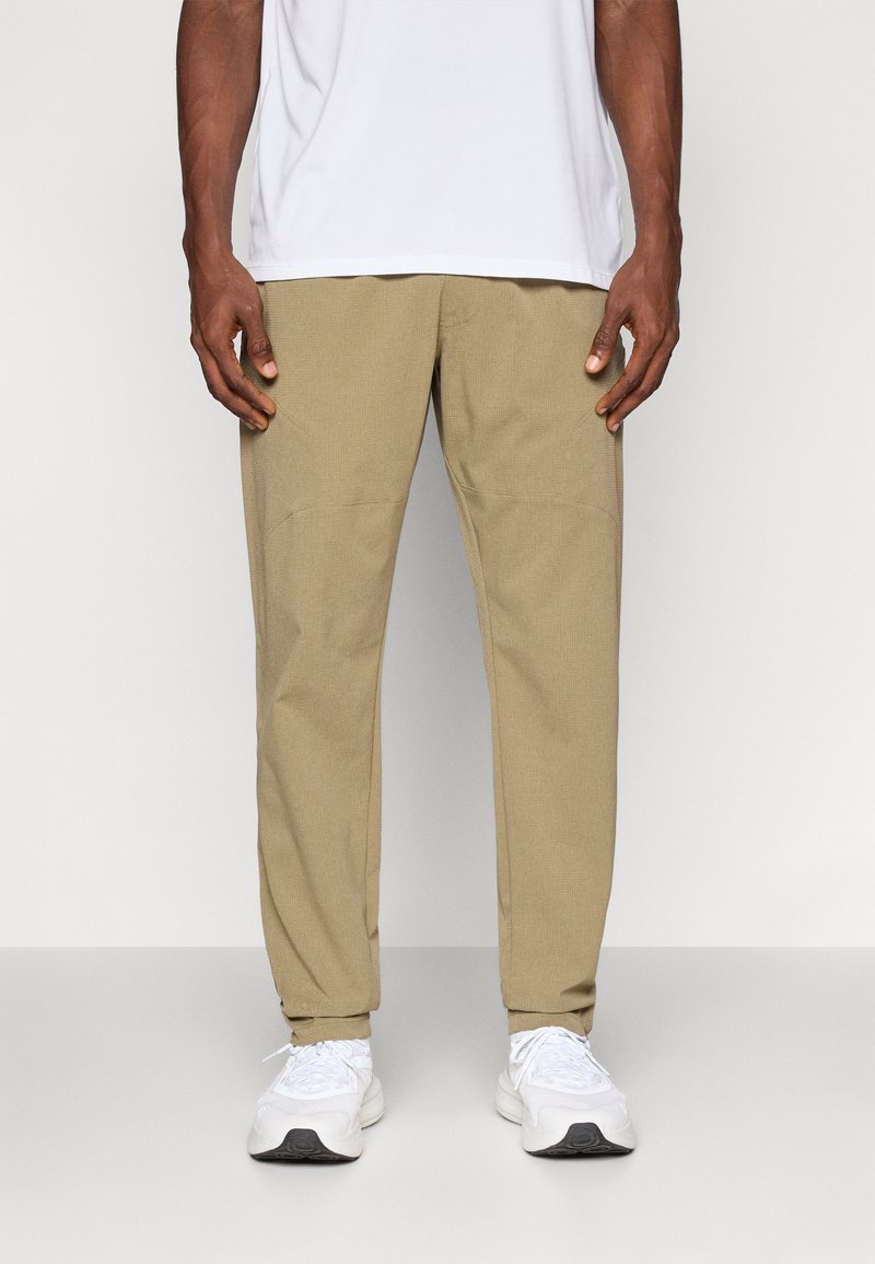 Hellbraune, tapered Hosen aus strukturiertem Stoff mit glattem Bund und elastischen Bündchen, kombiniert mit weißen Sportschuhen.