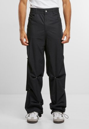 Black pants with a relaxed fit, featuring front pockets, a button closure, and unique fabric detailing with gathered sections near the ankles.