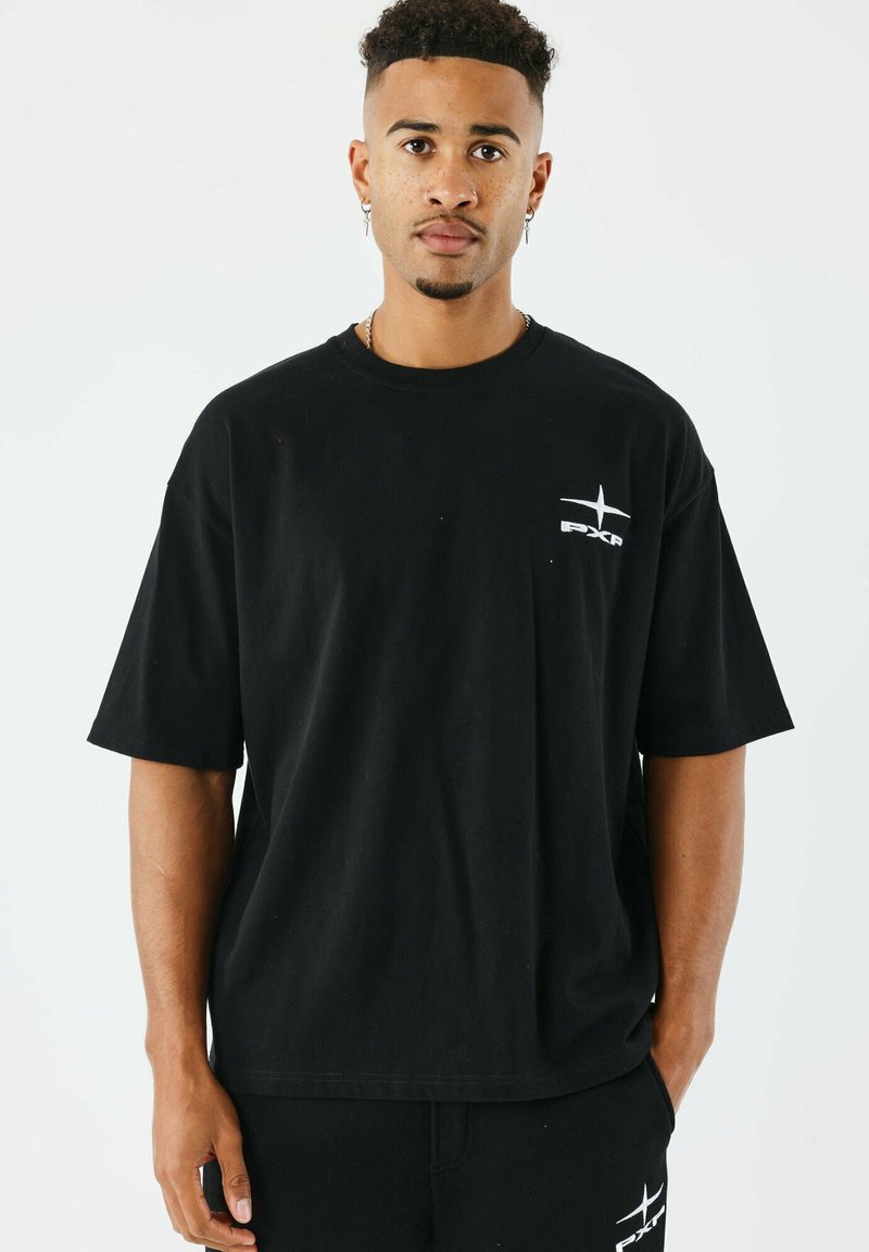 Camiseta de algodón negra con mangas cortas, cuello redondo, que presenta un logo blanco en el lado izquierdo del pecho y un corte relajado.