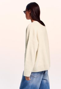 Maglione over-size color crema con orlo e polsini a coste, realizzato in materiale morbido. Abbinato a jeans blu larghi.