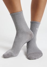 Calcetines gris ribeteados con un ligero brillo, que presentan un logo en el puño y una altura que llega a la mitad de la pantorrilla, hechos de un material suave y elástico.