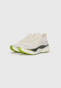 Pair of cream and black athletic shoes with green soles, mesh upper, laces, and brand logo on the side and tongue.