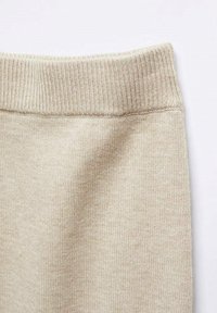Ceinture côtelée beige d'un vêtement en tissu, présentant une texture douce et un design sans coutures, affichée sur un fond clair.