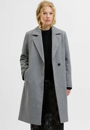 Manteau en laine gris avec un col cranté, fermeture à un bouton, et poches latérales, porté sur un pull en maille noir et une jupe en dentelle.