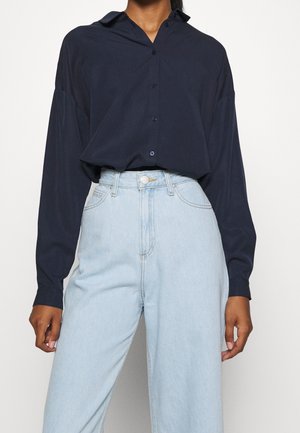 Marineblauwe langeknopshemd met een puntkraag, knoopsluiting aan de voorkant en een relaxte pasvorm, gecombineerd met lichtblauwe hoge taille jeans.