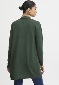 Cardigan verde con una vestibilità morbida, maniche lunghe e orlo a coste. Il tessuto a maglia è morbido, progettato per essere indossato sopra una camicia con colletto.