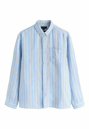 Mężczyzna z krótkimi brązowymi włosami i brodą, ubrany w jasnoniebieską, zapinaną na guziki koszulę w paski z kieszenią na piersi, patrzący lekko w lewo na jednolitym tle.