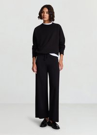 Sweat-shirt noir court avec un col rond, associé à un pantalon noir à jambes larges. Le mannequin porte des mocassins noirs. Tissu uni texturé.