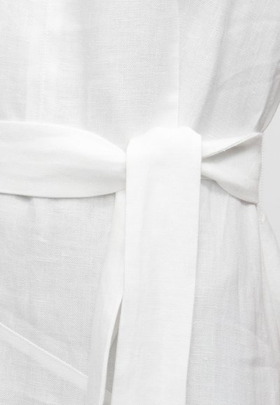 Κοντινό πλάνο μιας λευκής υφασμάτινης ζώνης δεμένης με απλό κόμπο γύρω από ένα υφασμάτινο λευκό ένδυμα με υφή.