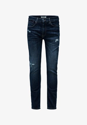 Vaqueros ajustados de color azul oscuro con ligeros parches desgastados en el muslo y la rodilla, con bolsillos frontales y trabillas para el cinturón.