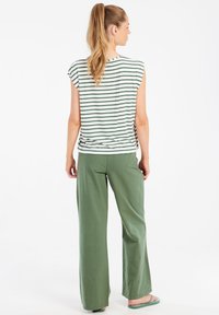 Gestreepte witte en groene T-shirt met kapmouwen, gecombineerd met losse groene broek. Omgekeerde groene sandalen, soepel van textuur, casual ontwerp.