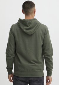 Oliven grøn hættetrøje lavet af blødt stof, med hætte, lange ærmer og en afslappet pasform. Simpel design uden synlige logoer eller mønstre.