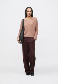 Světle růžový pletený svetr s dlouhými rukávy, kombinovaný s vysokými širokými bordó kalhotami. Černá kabelka přes rameno a černé boty.