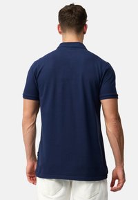 Marineblå polo skjorte med korte ærmer, ribbet krave og sideslits. Laget av teksturert stoff, med et merke på nedre søm.