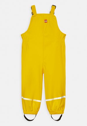 Gul vattenavvisande overall med justerbara axelremmar, elastiska muddar, reflexstripes och LEGO-logotyp på framsidan.