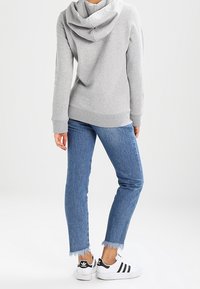 Grijze hoodie met ribgebreide manchetten, gecombineerd met lichtblauwe denimjeans met rafelige zoom en zwart-witte sportschoenen.