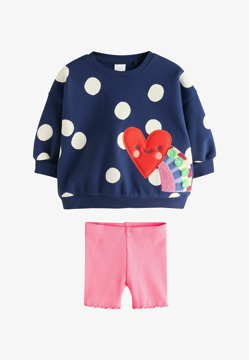 Sweat-shirt bleu marine à pois blancs avec un patch en forme de cœur rouge souriant, associé à un short rose à côtes avec des bords festonnés.