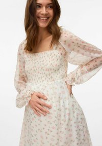 Robe florale légère et transparente avec un décolleté carré, un corsage smocké, des manches longues et des poignets volantés. Présente une palette de couleurs pastel.