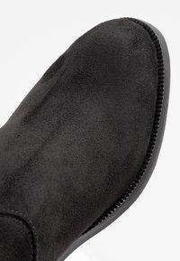 Schwarze Wildleder-Stiefelette mit runder Zehe und strukturierter Oberfläche. Verfügt über eine glatte schwarze Sohle und dezente vertikale Nähte an der Seite.