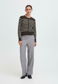 Brun stripete cardigan med knapper, båret over lyse grå høyt liv bukser, kombinert med svarte høyhælte sko. Glatt strikket tekstur.