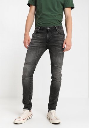 Jeans negros slim fit con textura desgastada, costuras detalladas y un diseño clásico de cinco bolsillos, combinados con zapatillas blancas.