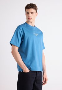 Kék pamut póló rövid ujjal és kerek nyakkivágással, az elején hímzett "Calvin Klein Jeans" logóval.
