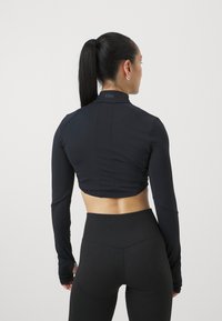 Svart, kortermet langermet treningsgenser med høy krage, strukturert bakpanel og tettsittende design, kombinert med høyt midjesvart tights.