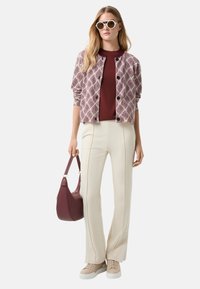 Red and white patterned jacket, maroon top, cream trousers, beige sneakers, and a burgundy handbag; sunglasses with white frames.