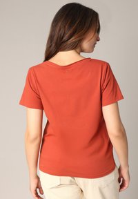 Roestkleurig, kortgevoerd T-shirt met een ontspannen halslijn en subtiele details op de achterkant. Zachte, gladde stoftextuur.