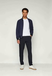 Navy bomber jacket over a white t-shirt, paired with dark pants and white sneakers. Smooth fabric with a fitted design and clean lines.