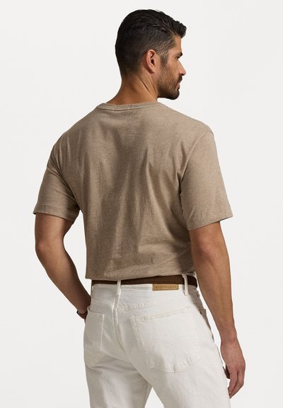 T-shirt marron à manches courtes avec un col rond, fabriqué en tissu doux. Stylisé avec un pantalon blanc et une ceinture marron. Vue de dos, montrant une coupe décontractée.