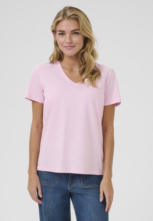 T-shirt en coton rose clair avec un col en V, des manches courtes et un ourlet droit. Associée à un jean en denim bleu ; coupe décontractée et texture douce.