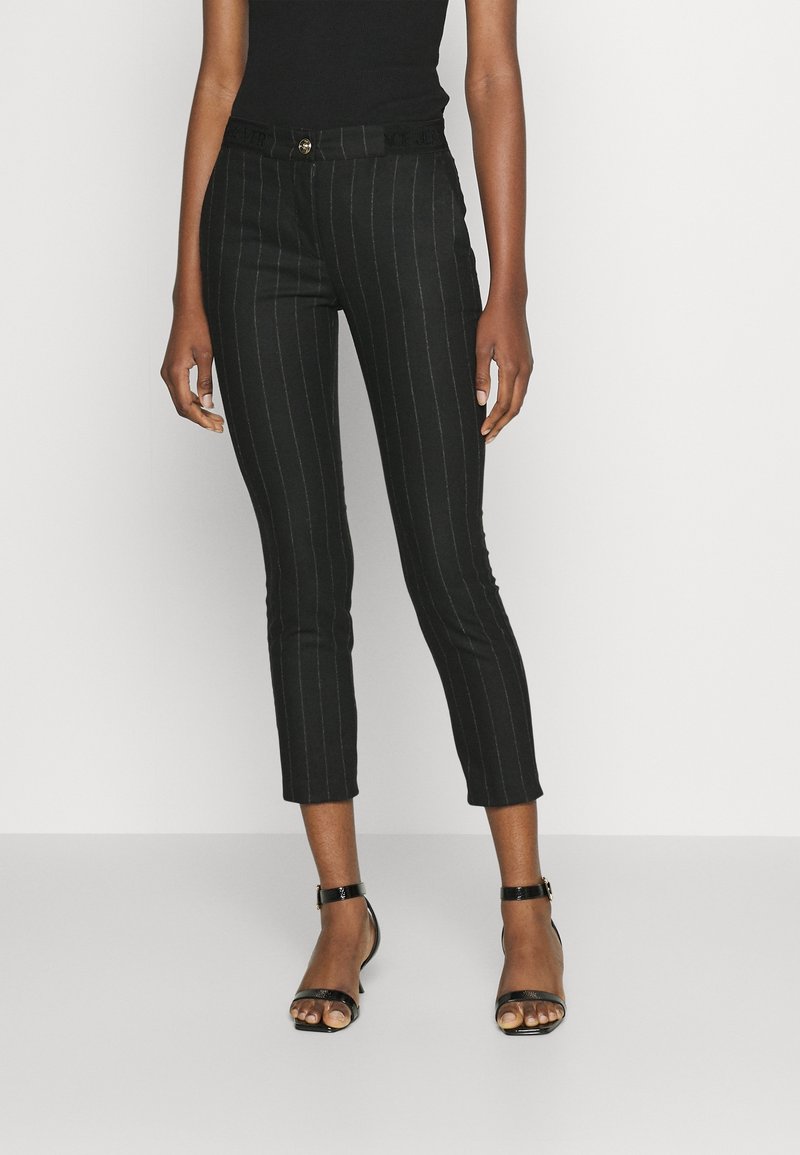 Black pinstriped cropped pants with a fitted design, made from a smooth fabric, featuring a gold button and a branded waistband.