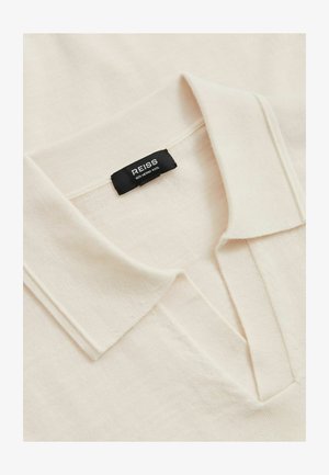 Cremefarvet polo-shirt lavet af 100% merinould, med en blød tekstur, en foldet krave og en afslappet pasform. Mærket viser brandnavnet.