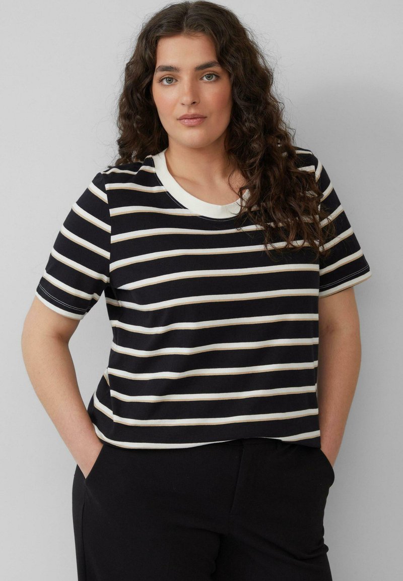 Zwart-wit gestreept T-shirt met korte mouwen en een ronde halslijn, afgewerkt met contrasterende crèmekleurige randen. Zachte stof. Model heeft de handen in de zakken.