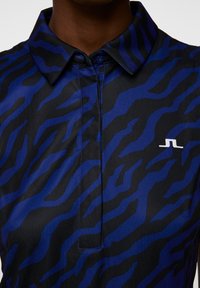 Short-sleeve polo shirt in smooth fabric featuring a bold, blue and black tiger stripe pattern; collar with button closure; small logo on chest.