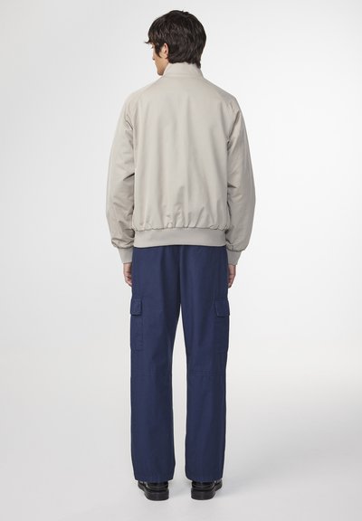 Giacca bomber beige con un colletto alto e polsini elasticizzati, abbinata a pantaloni cargo blu navy con grandi tasche laterali e vestibilità comoda.