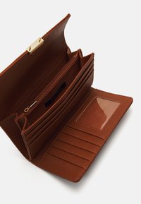 Portefeuille en cuir texturé marron avec un fermoir doré, plusieurs emplacements pour cartes, une poche zippée et un emplacement transparent pour une pièce d'identité. Design spacieux et pratique.