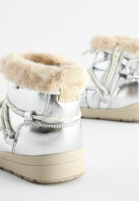 Silverfärgade, metalliska ankelboots med krage av fuskpäls, mocka-accenter, snördesign och en texturerad beige sula.